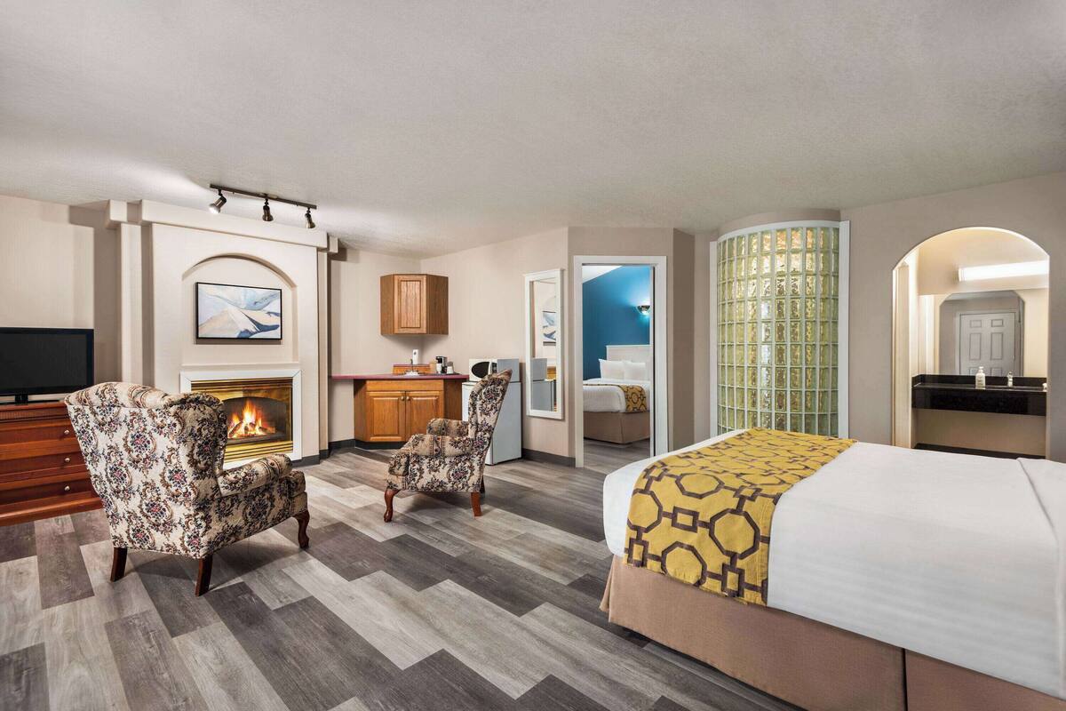 Une chambre d’hôtel avec une cheminée, un lit recouvert d’une couvre-lit à motifs, une chaise et un bureau avec une télévision.