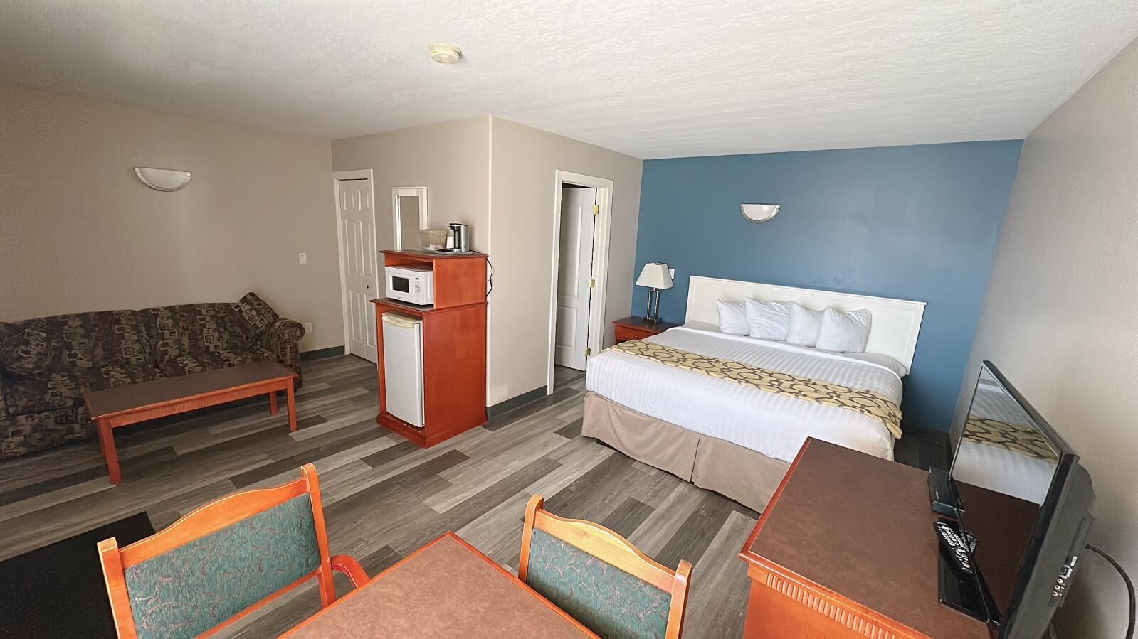 A hotel room with a bed, a desk, a chair, a microwave, a small refrigerator, a sofa, and a television.