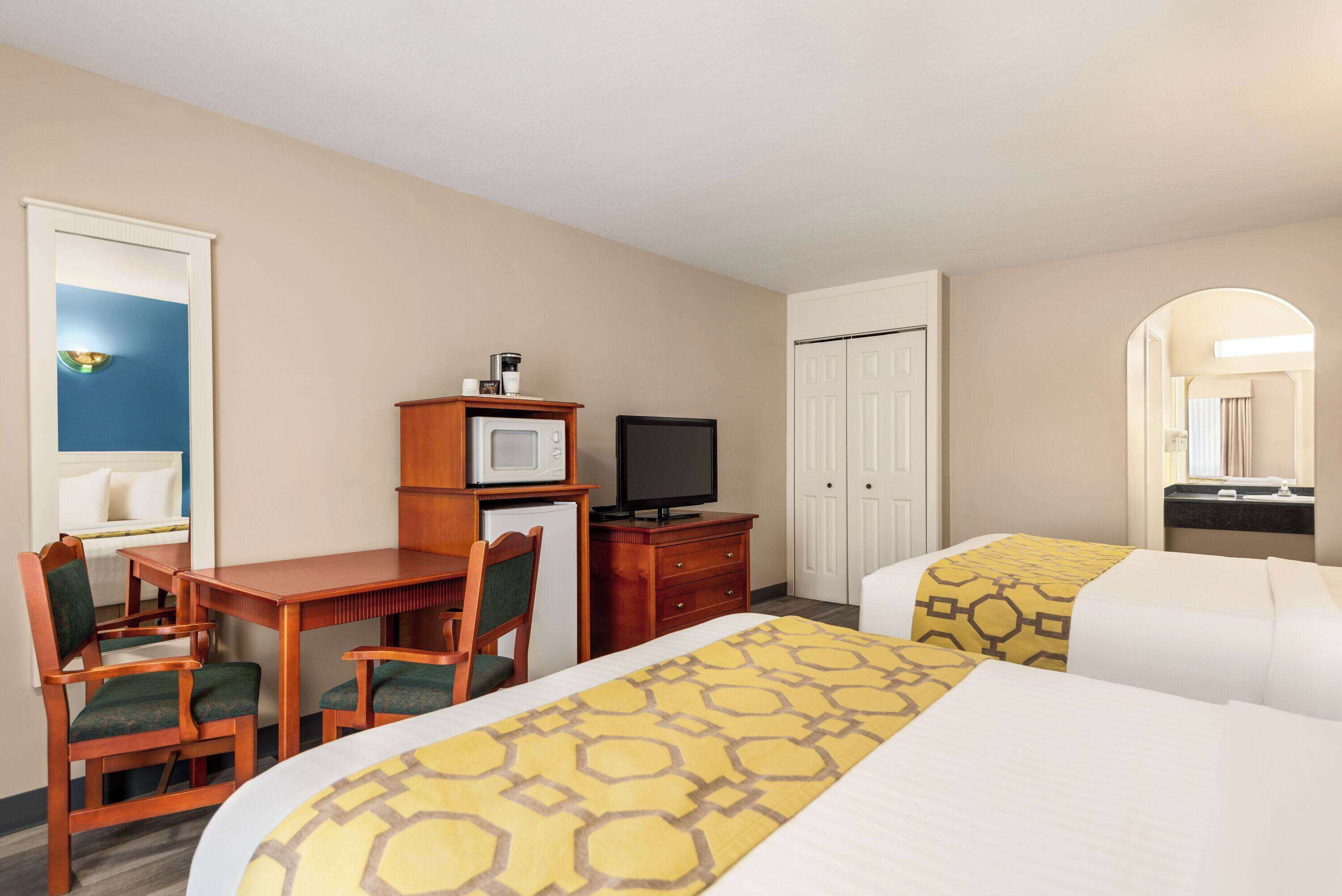 A hotel room with two beds, a desk with a television, a microwave, and a small refrigerator.