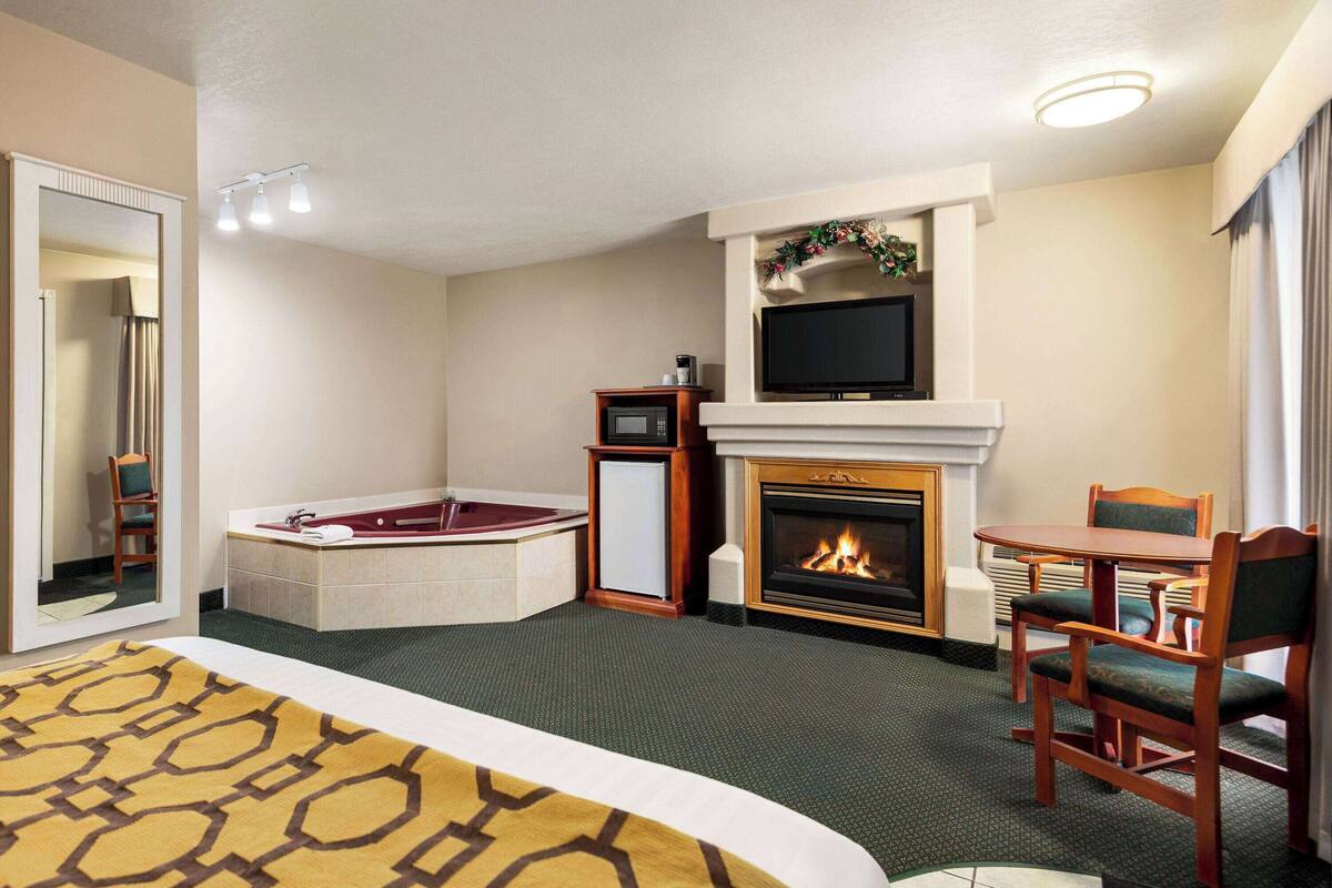 Une chambre d’hôtel avec un grand lit, une cheminée, une télévision, une petite table avec des chaises et une baignoire.