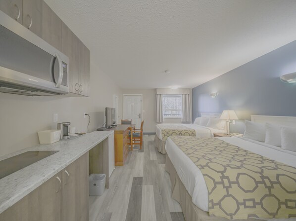 A hotel room with a kitchenette, two beds, a desk, and a window with curtains.