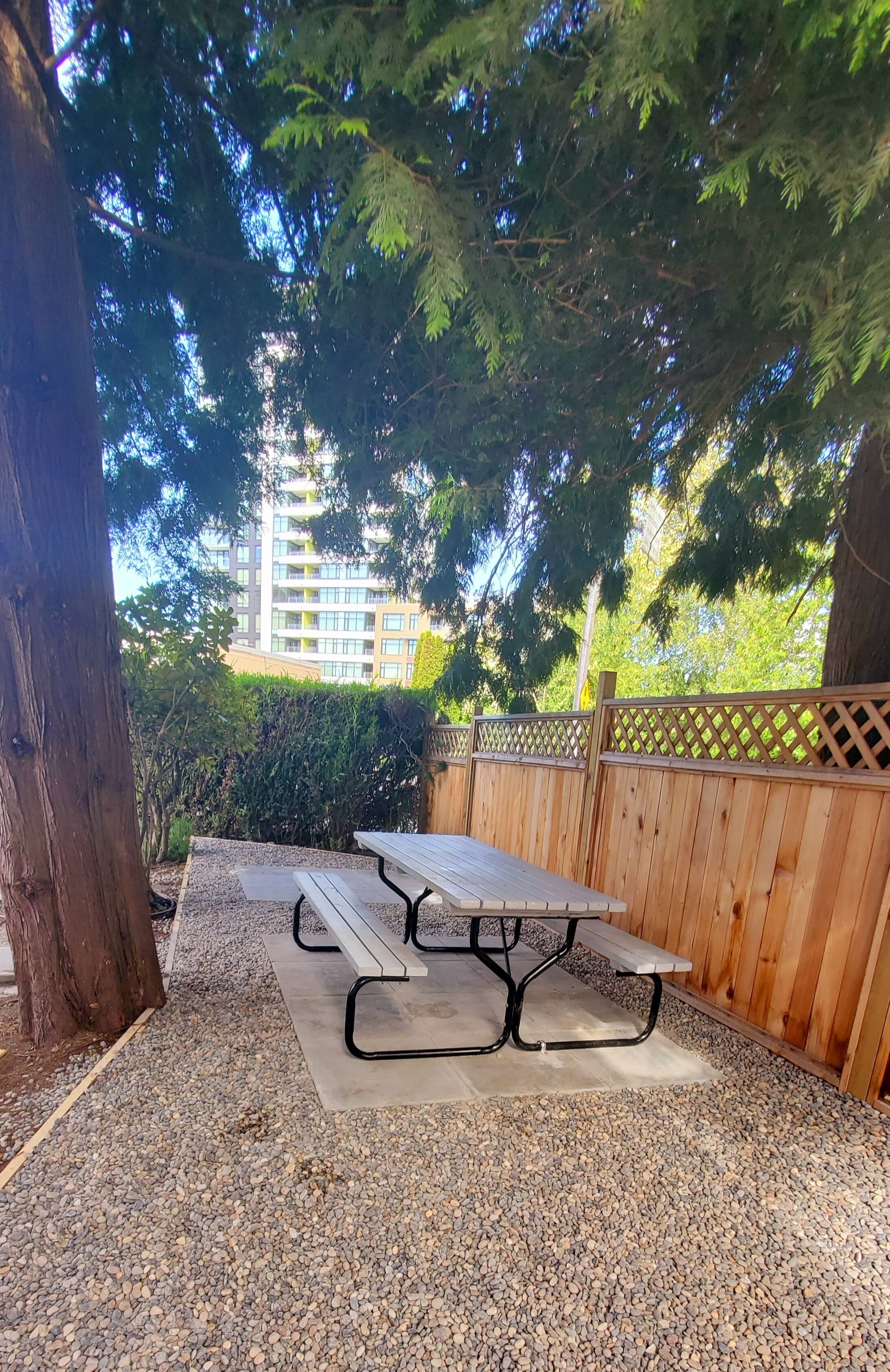 Una mesa de picnic de madera con bancos, rodeada de grava y una cerca de madera.