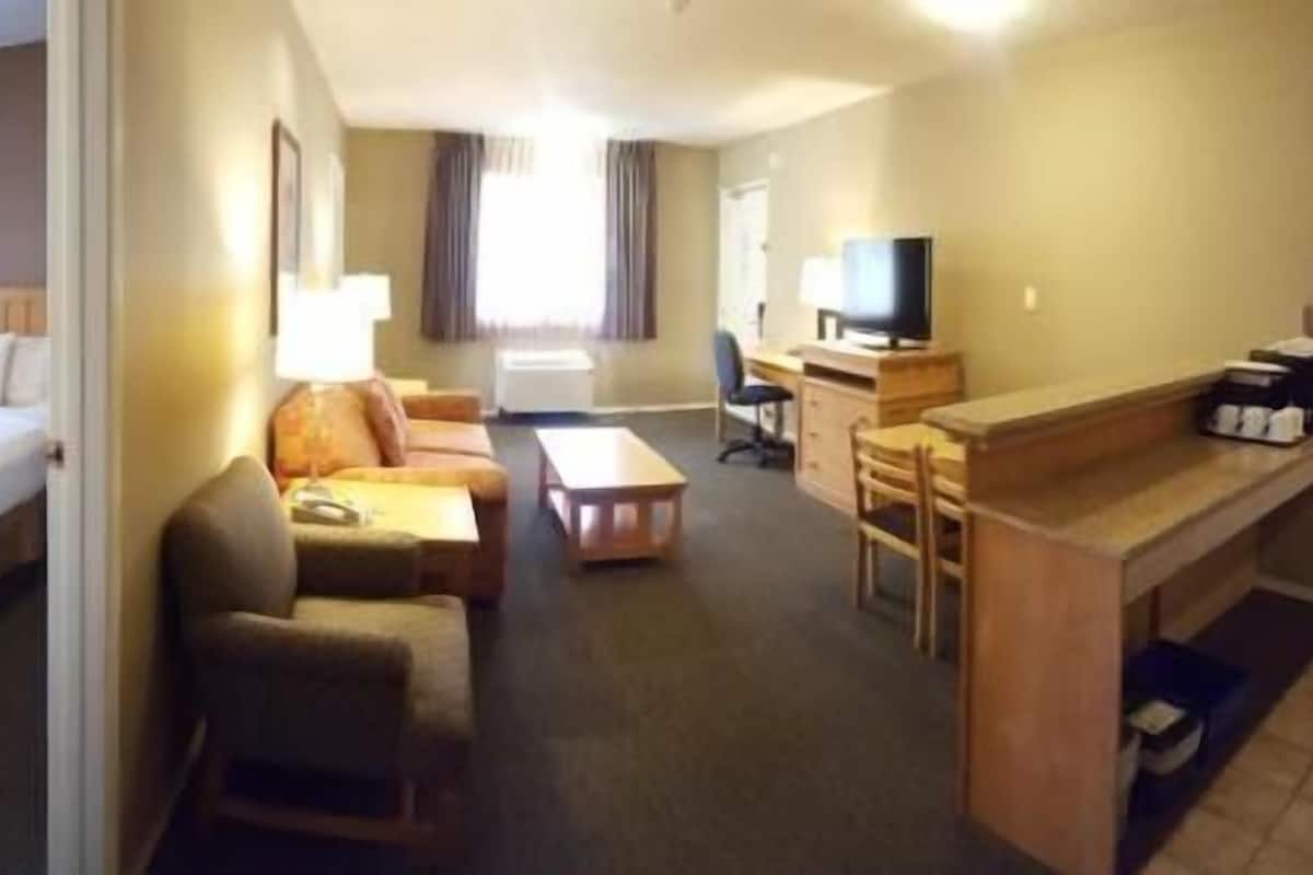 A hotel room with a bed, a sofa, a desk, a chair, a TV, and a lamp.