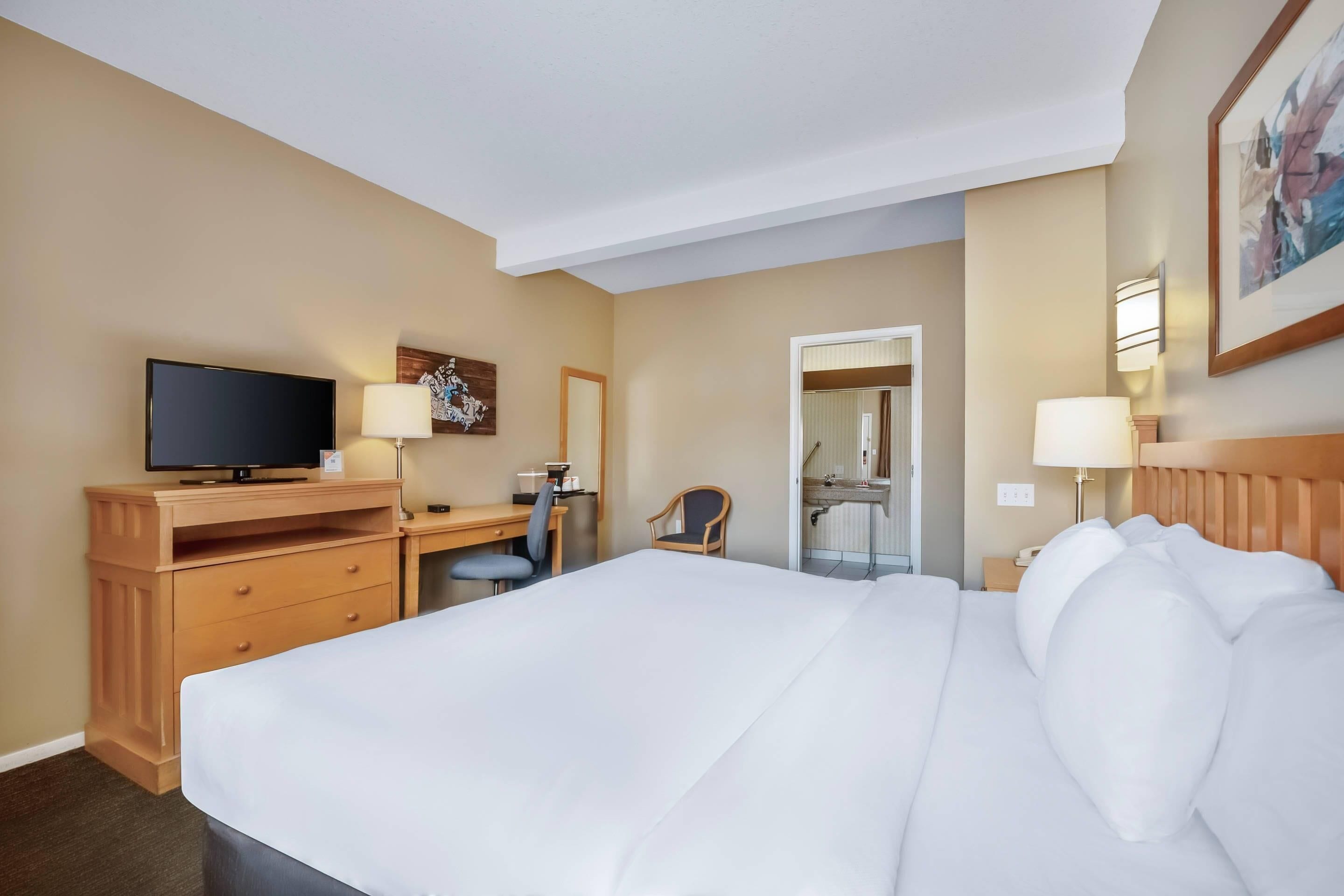 A hotel room with a large bed, a desk with a television, a chair, and a bathroom visible through an open door.