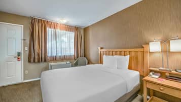 Una habitación de hotel con una cama grande, cabecera de madera, escritorio con lámpara, una silla y ventana con cortinas.