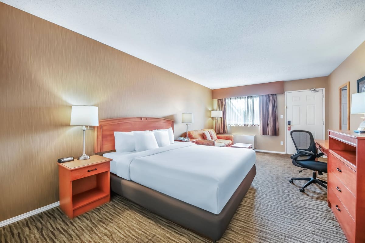 A hotel room with a large bed, a desk, a chair, and a dresser.