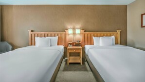 Une chambre d’hôtel avec deux lits, une tête de lit en bois, une table de chevet avec des lampes et une petite table.