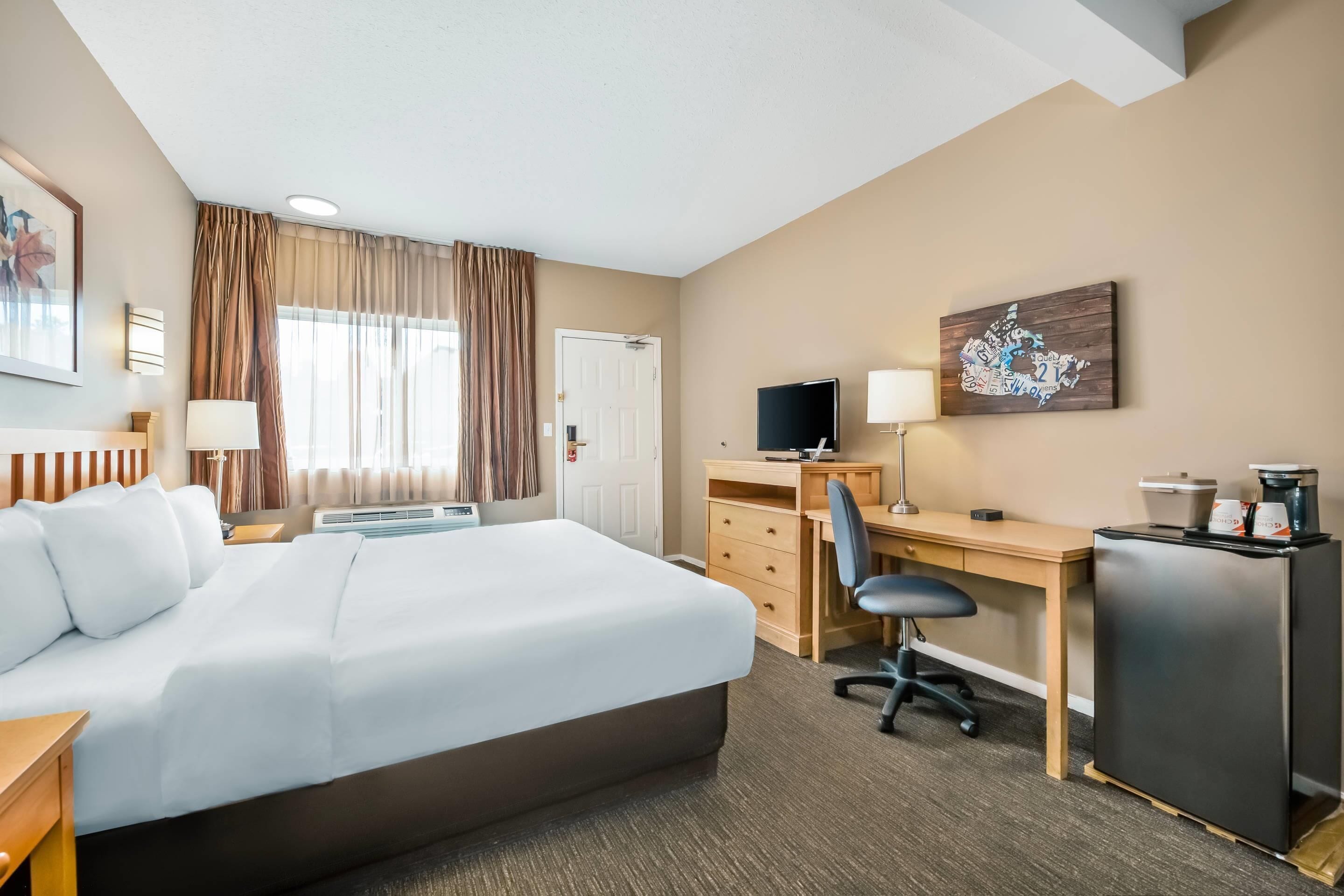 A hotel room with a large bed, a desk, a chair, a TV, a coffee maker, and a refrigerator.