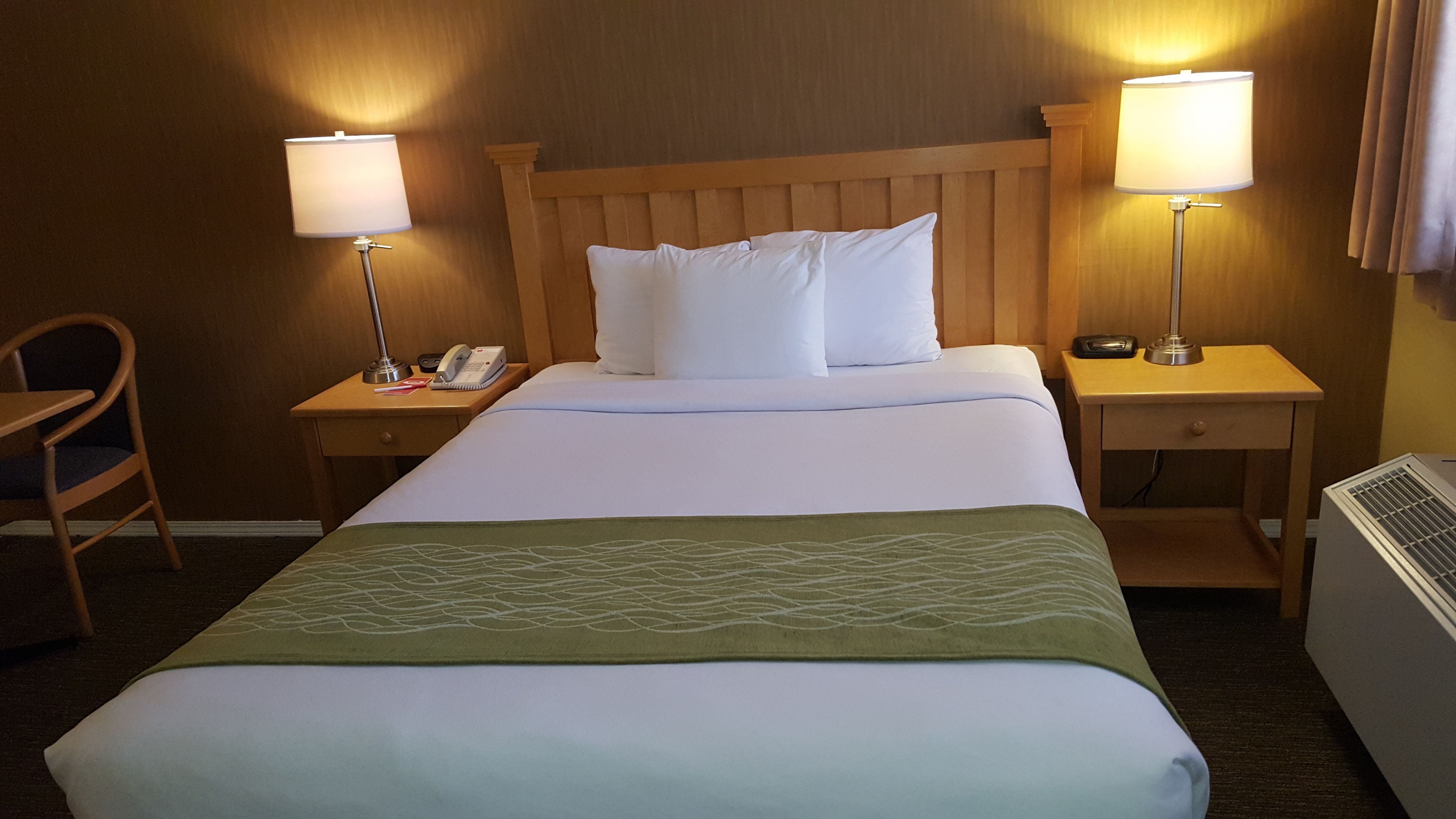 Ein Hotelzimmer mit einem Bett, zwei Nachttischen mit Lampen, einem Sessel und einer Klimaanlage.