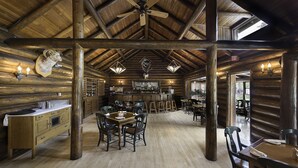 A rustic wooden interior with a bar area, dining tables, and a ceiling fan.