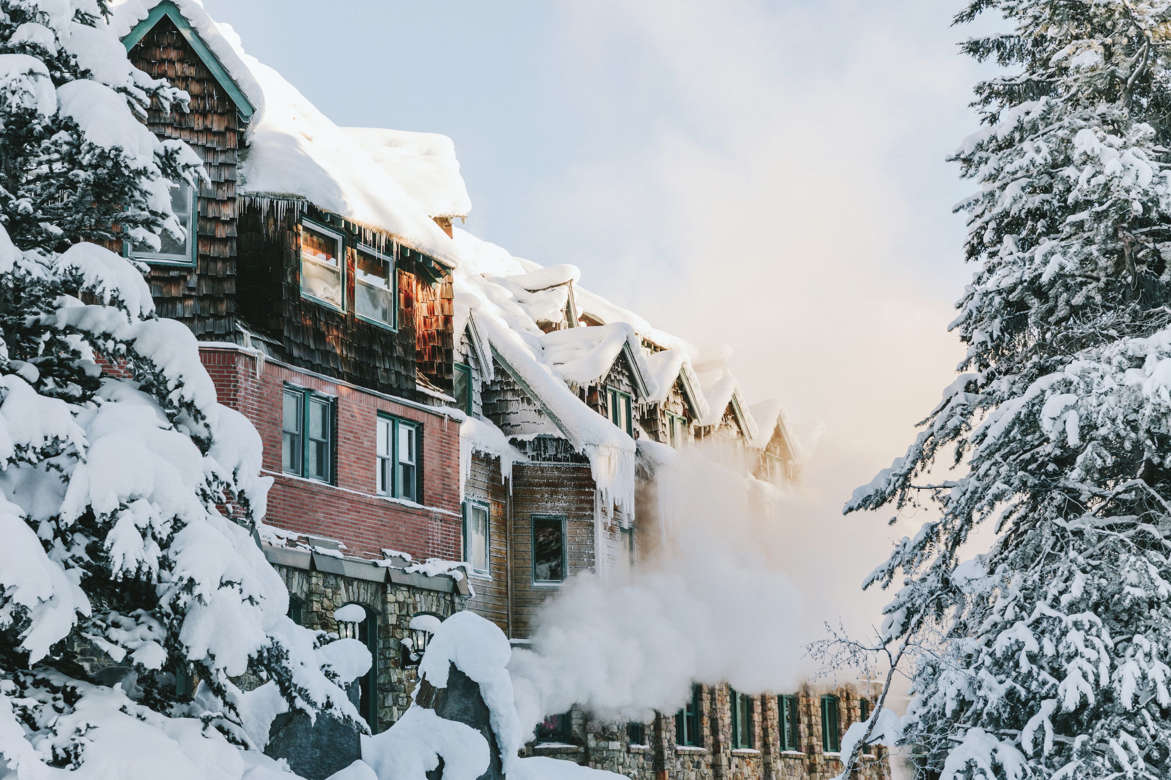 Un bâtiment enneigé, avec une cheminée d’où s’échappe de la fumée, entouré d’arbres chargés de neige.