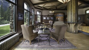 A room with a large window, wooden beams, a table with chairs, and a patterned rug.