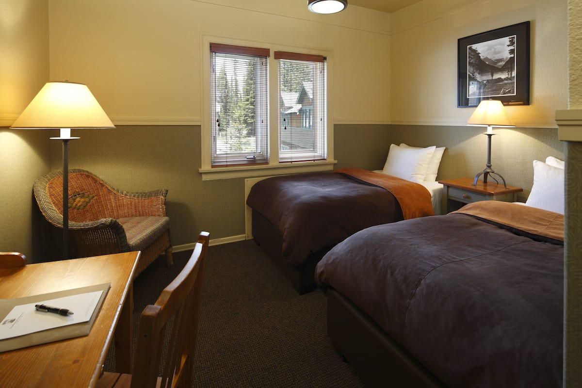 A hotel room with two beds, a desk, a chair, and a window with blinds.