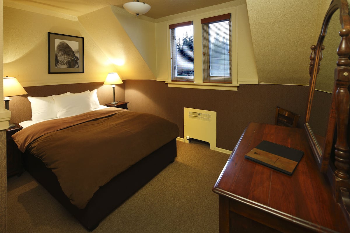 A bedroom with a bed, bedside table, lamp, and a dresser with a mirror.