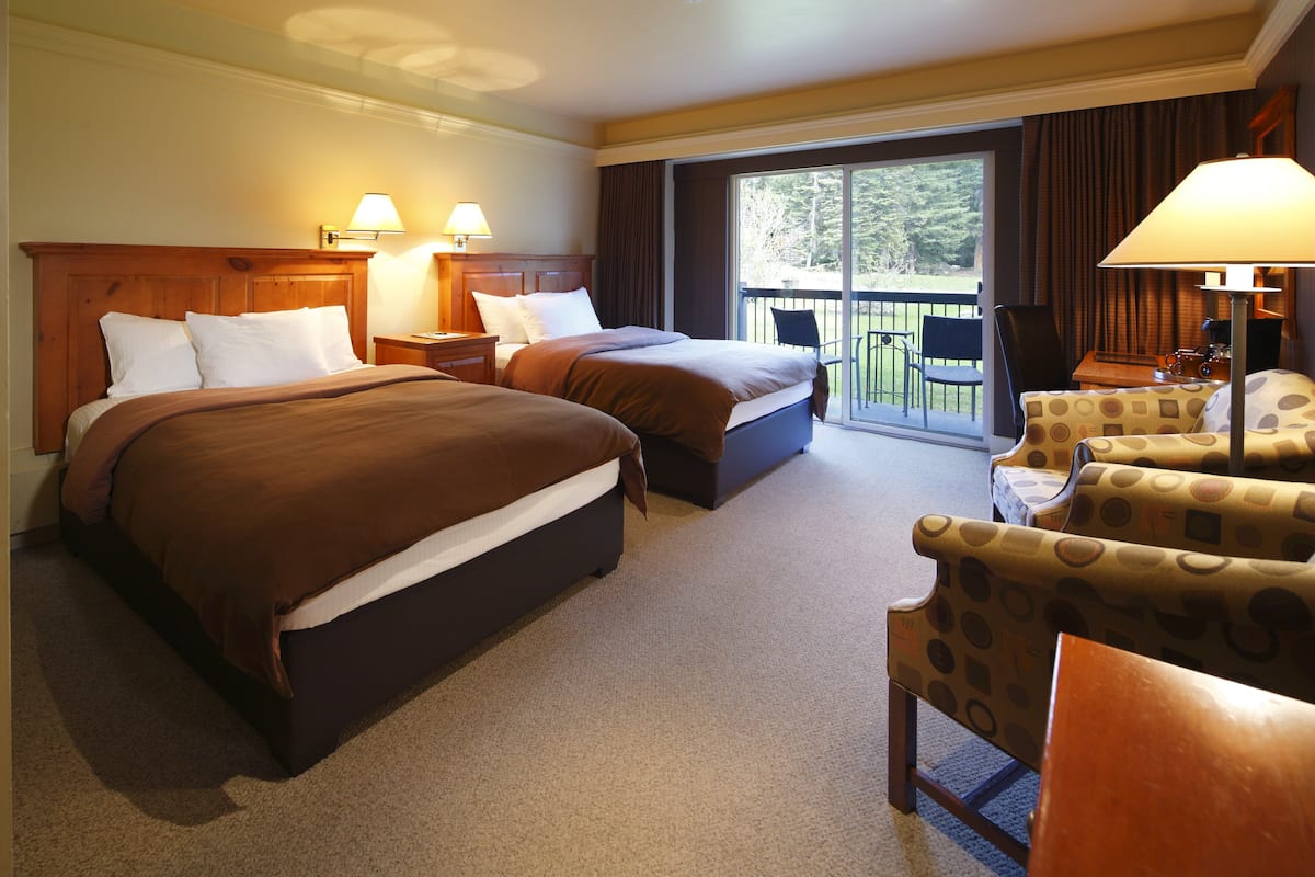 A hotel room with two beds, a balcony, and a seating area with patterned chairs.
