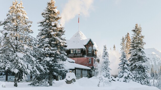 A snow-covered lodge with a prominent chimney, surrounded by evergreen trees.