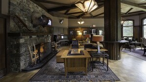 A cozy living room with a stone fireplace, wooden furniture, and a large window providing natural light.
