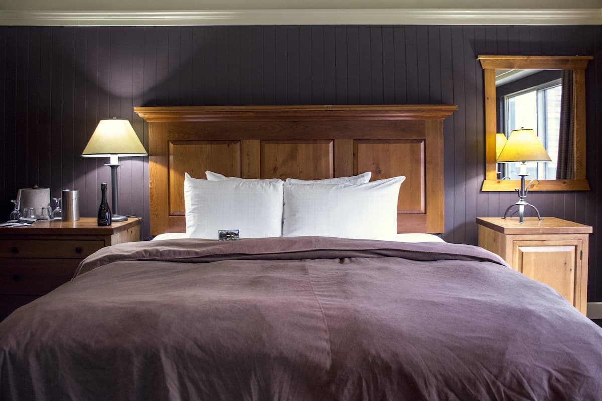 A neatly made bed with a wooden headboard, a bedside table with a lamp, and a mirror on the wall.
