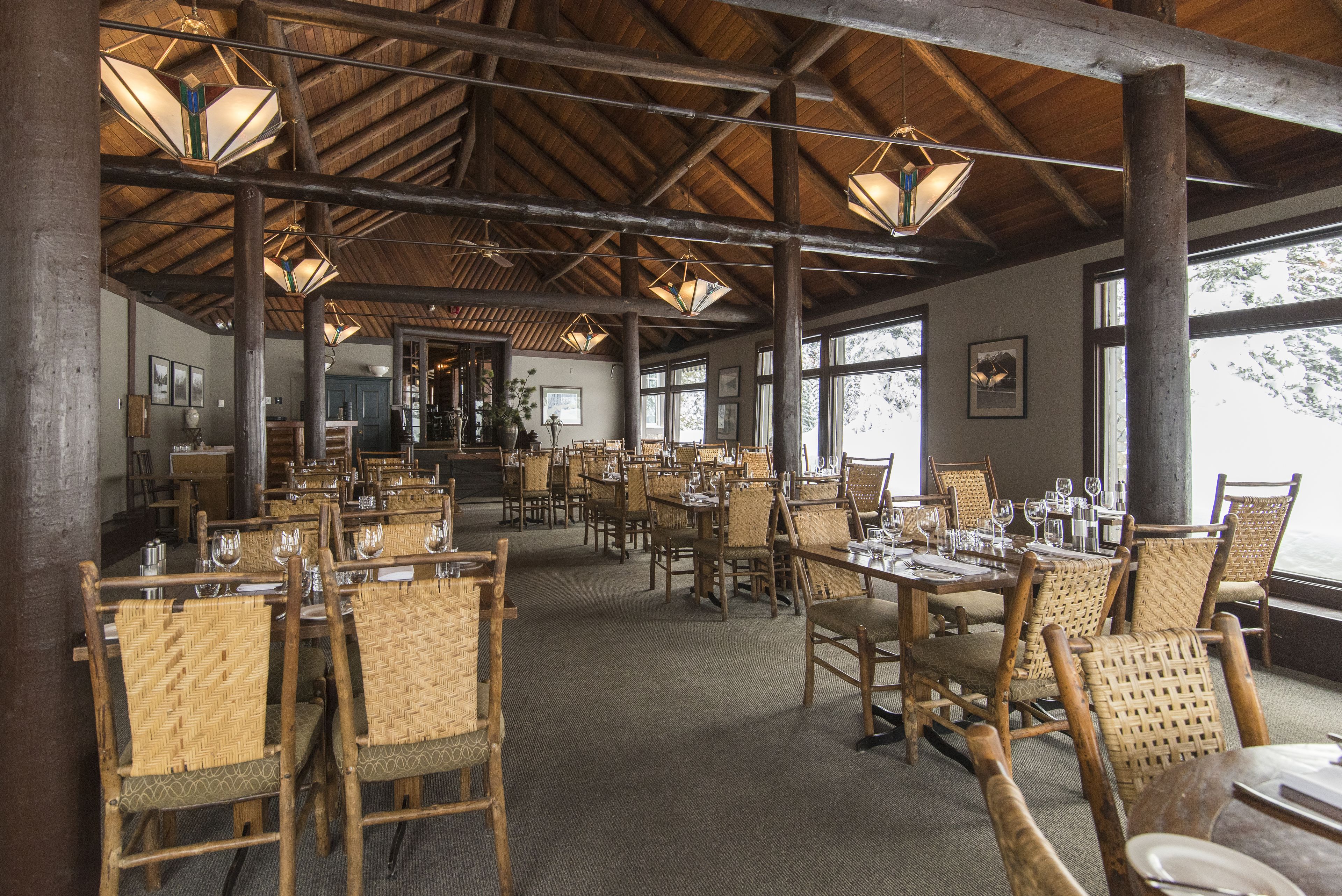 A spacious dining area with wooden tables and chairs, large windows, and a high ceiling with exposed beams.