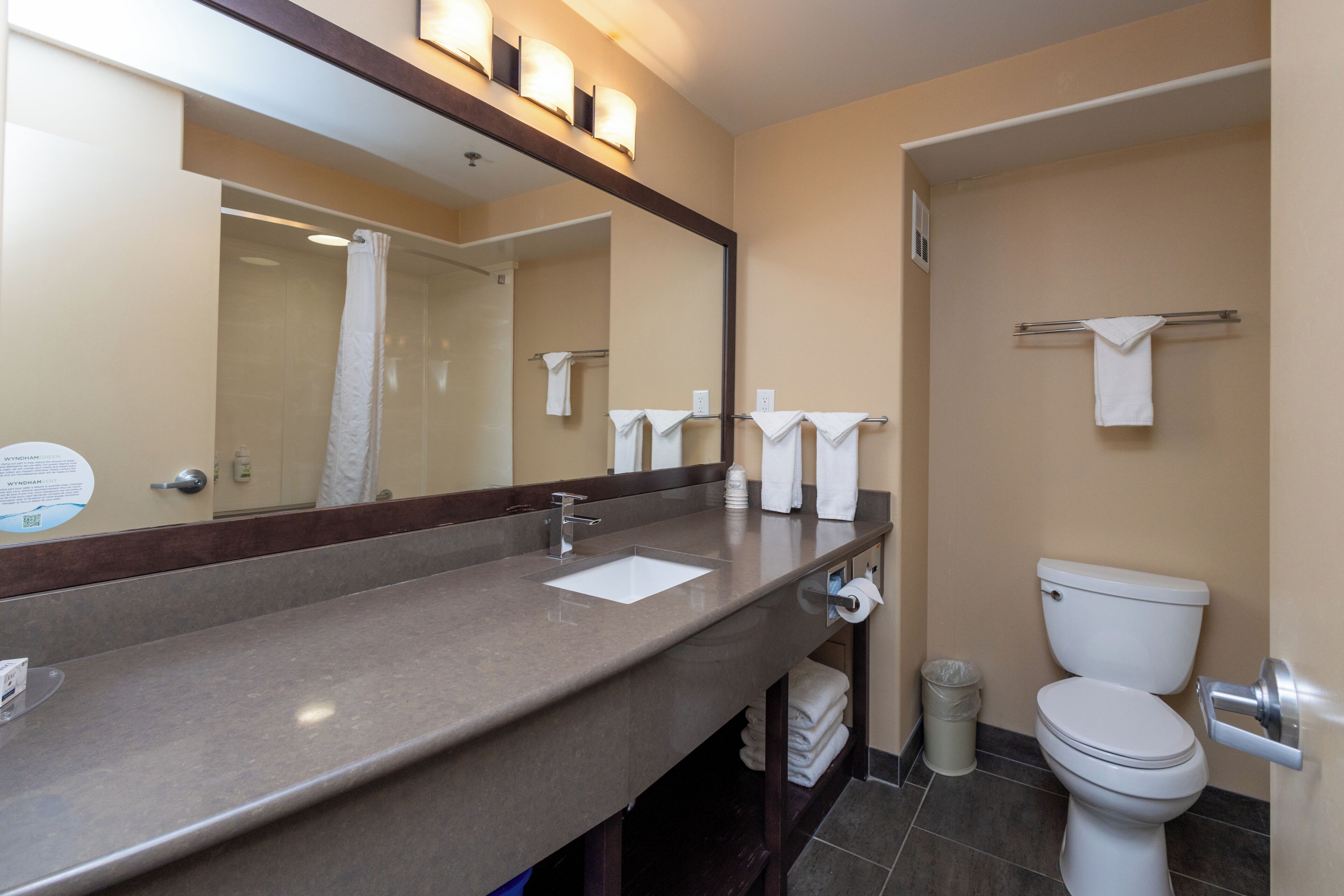 A bathroom with a sink, mirror, towel rack, toilet, and trash can.