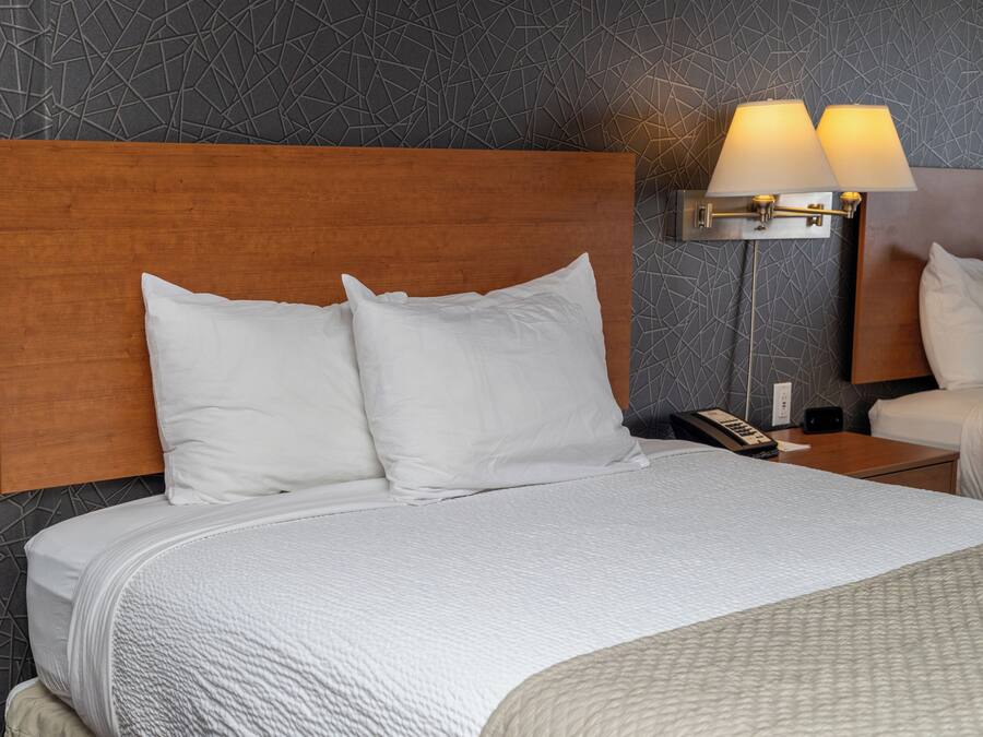 Une chambre d’hôtel avec une tête de lit en bois, du linge de lit blanc, une table de chevet avec une lampe et un téléphone.