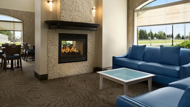 A cozy lounge area with a stone fireplace, blue leather sofa, and a glass coffee table. - Days Inn & Suites by Wyndham Brandon (Brandon)