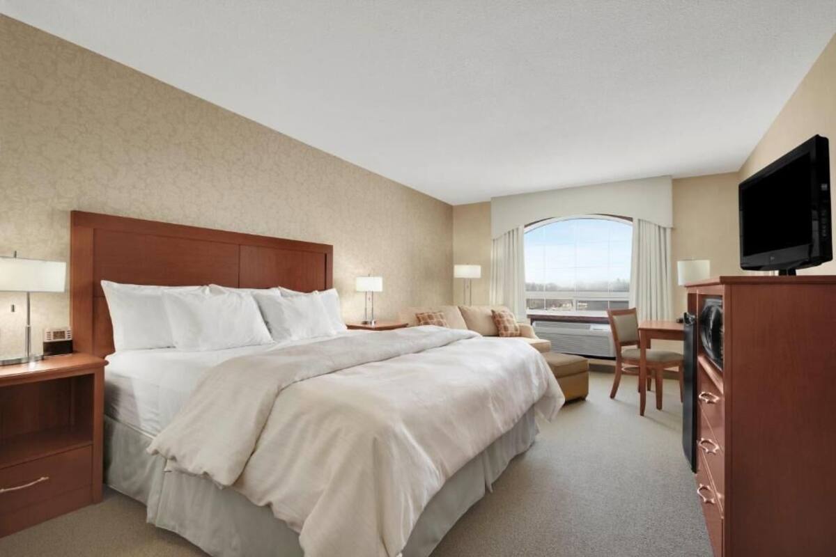 Une chambre d’hôtel avec un grand lit, une télévision, un bureau avec une chaise et une vue sur la ville par la fenêtre.