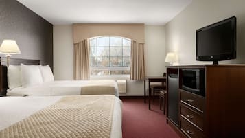 A hotel room with two beds, a desk, a television, and a window with curtains.