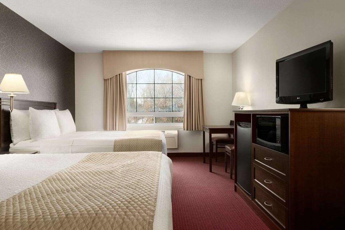 A hotel room with two beds, a TV, a desk, and a window with curtains.