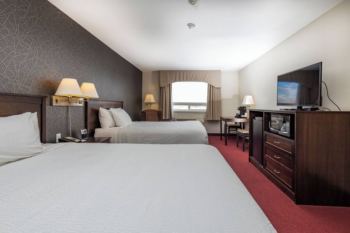 Une chambre d’hôtel avec deux lits, une télévision, un bureau avec une chaise et une fenêtre avec des rideaux.