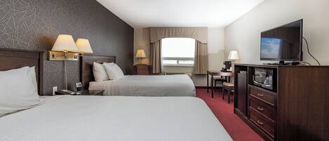 A hotel room with two beds, a television, a desk with a chair, and a window with curtains.