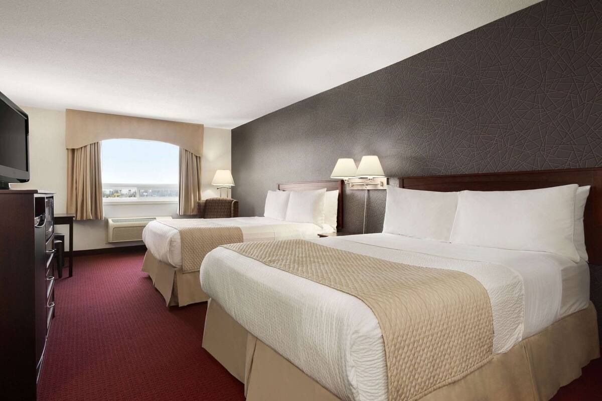 A hotel room with two beds, a TV, a desk, and a window with curtains.