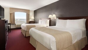 A hotel room with two beds, a TV, a desk, and a large window with curtains. - Days Inn & Suites by Wyndham Brandon (Brandon)
