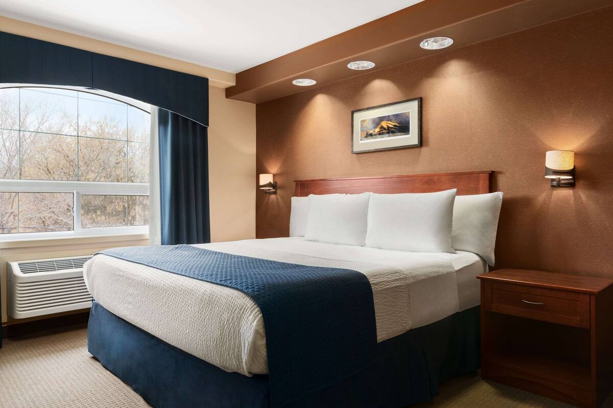 Une chambre d’hôtel avec un grand lit, une table de chevet, une lampe fixée au mur et une fenêtre avec des rideaux.