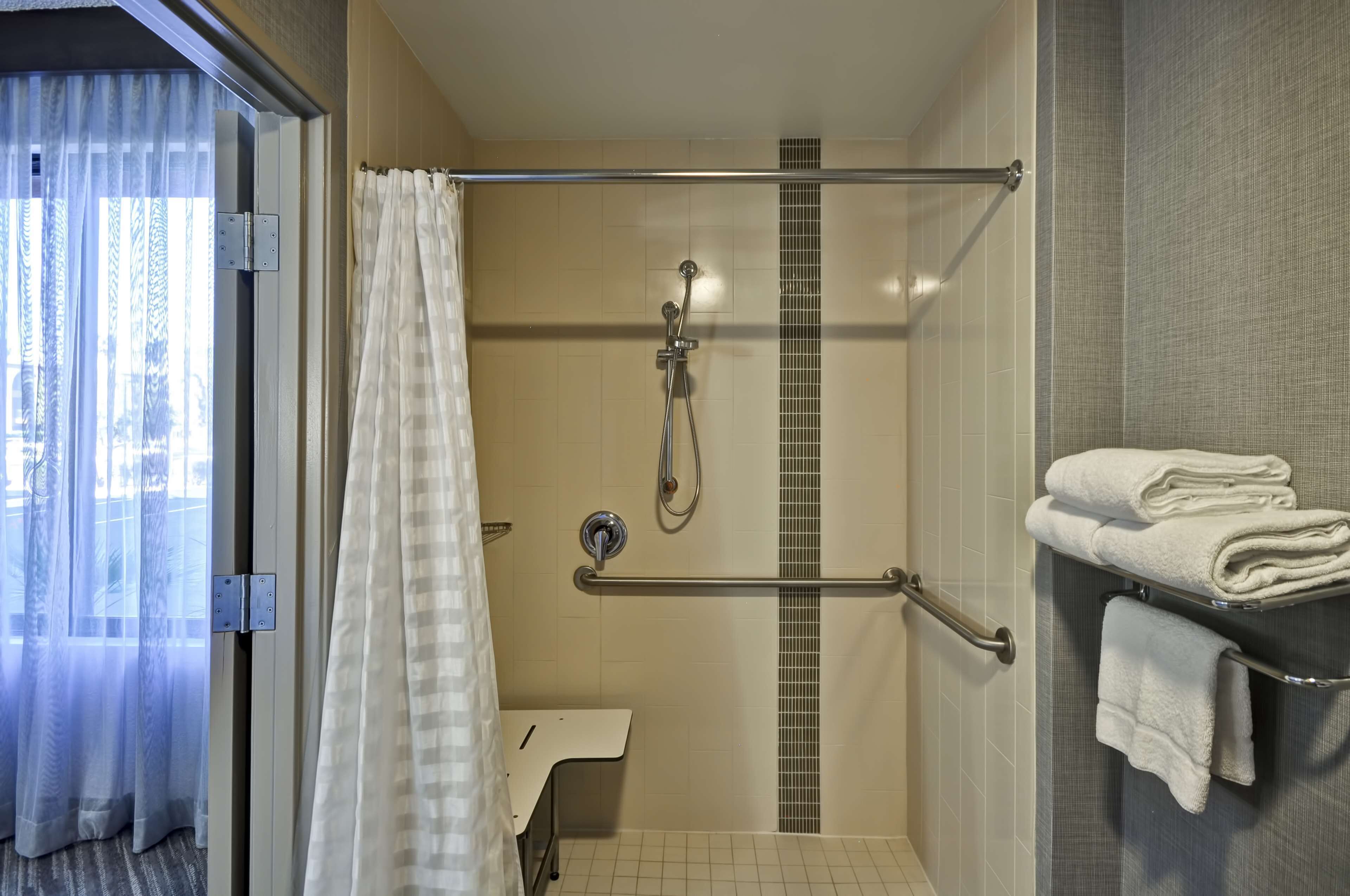 A shower area with a glass door, a towel rack with folded towels, and a showerhead.