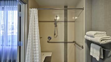 A shower area with a glass door, a towel rack with folded towels, and a showerhead.