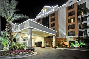 Un hotel Hyatt Place con facciata moderna, ingresso coperto e palme nel paesaggio.