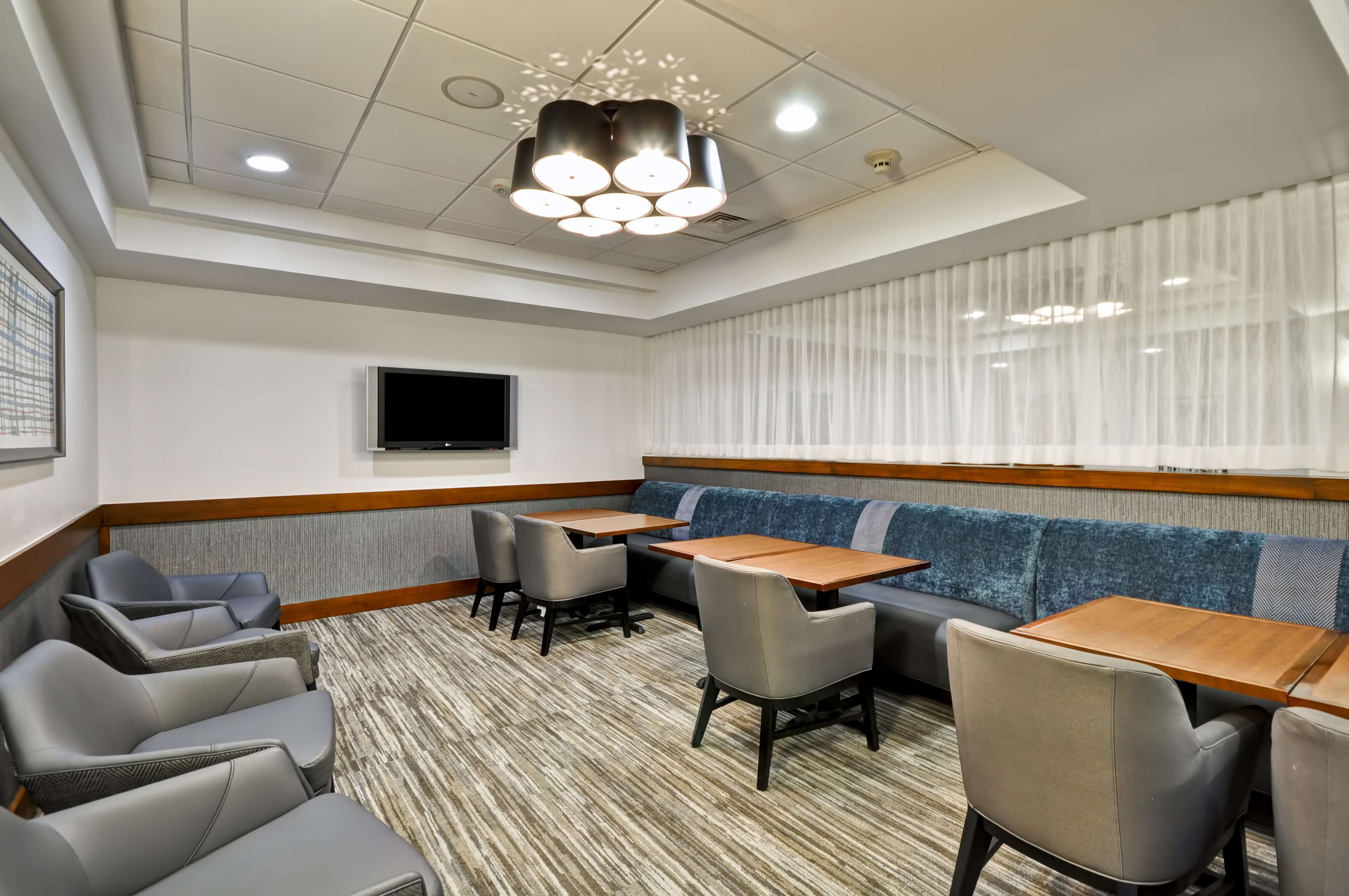 A hotel room with a seating area featuring a sofa and chairs, a flat-screen TV mounted on the wall, and a patterned carpet.