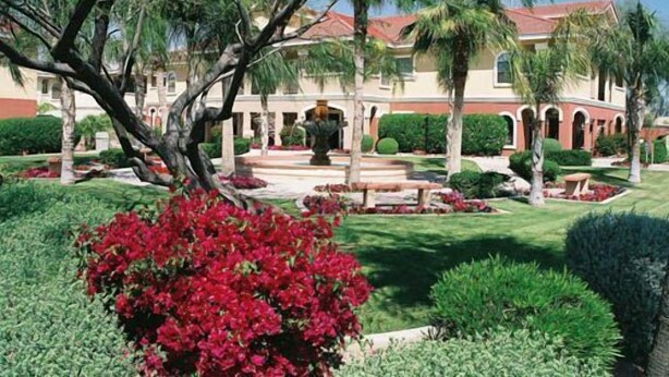 A landscaped garden with a fountain, palm trees, and a building with a red roof. - Westgate Painted Mountain Golf Resort (Mesa)