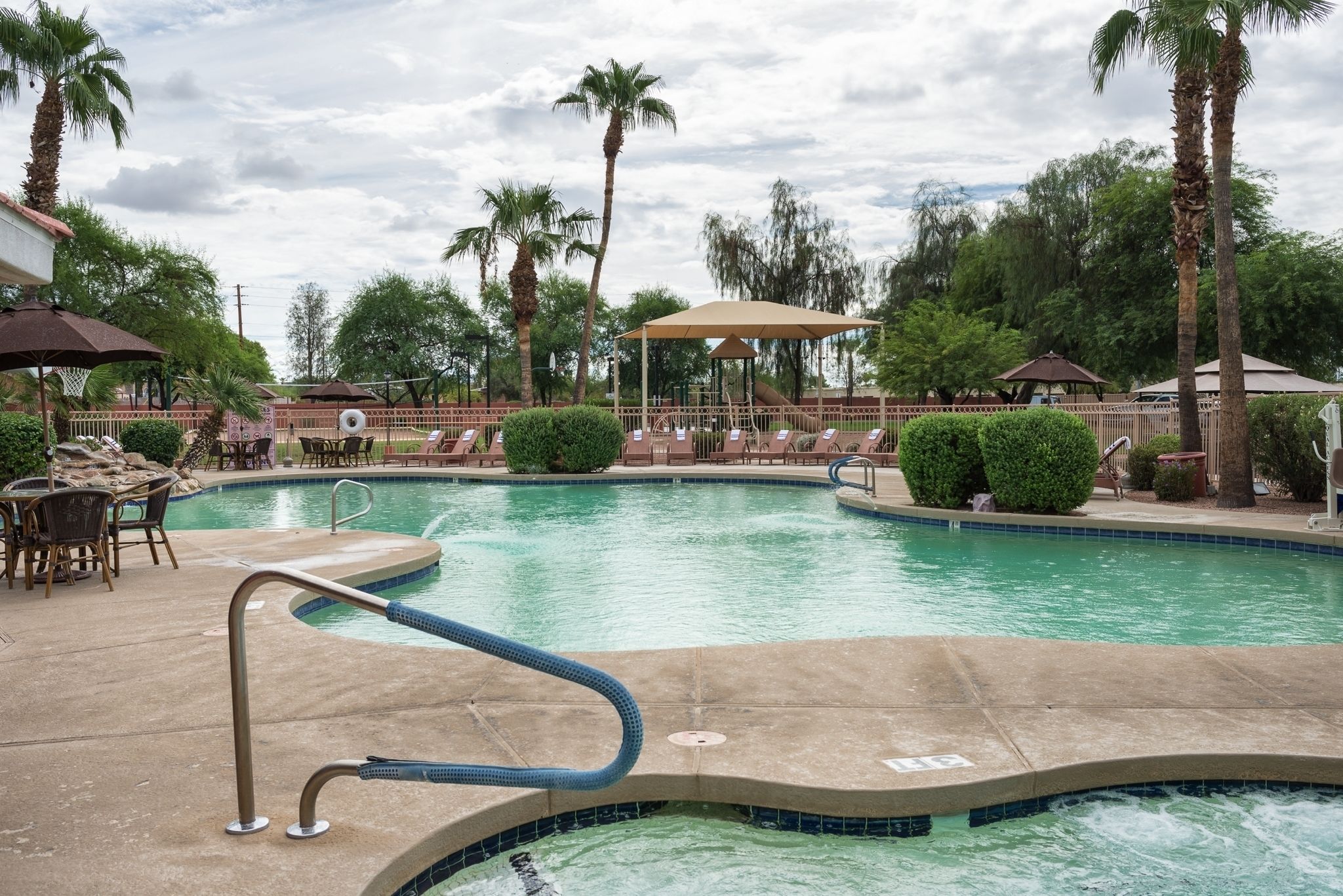 A swimming pool with lounge chairs and umbrellas, surrounded by palm trees and a gazebo.