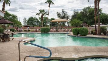 Una piscina con sillas de descanso y sombrillas, rodeada de palmeras y un pabellón.