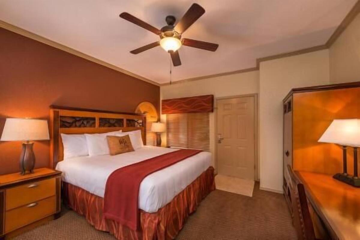 A hotel room with a bed, a nightstand, a desk, a chair, a ceiling fan, and a door.