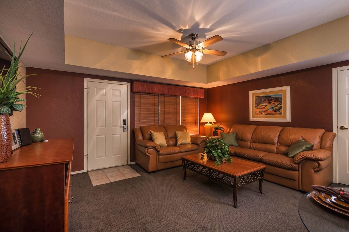 A living room with a brown leather sofa, a wooden coffee table, a ceiling fan, and a door with a window.