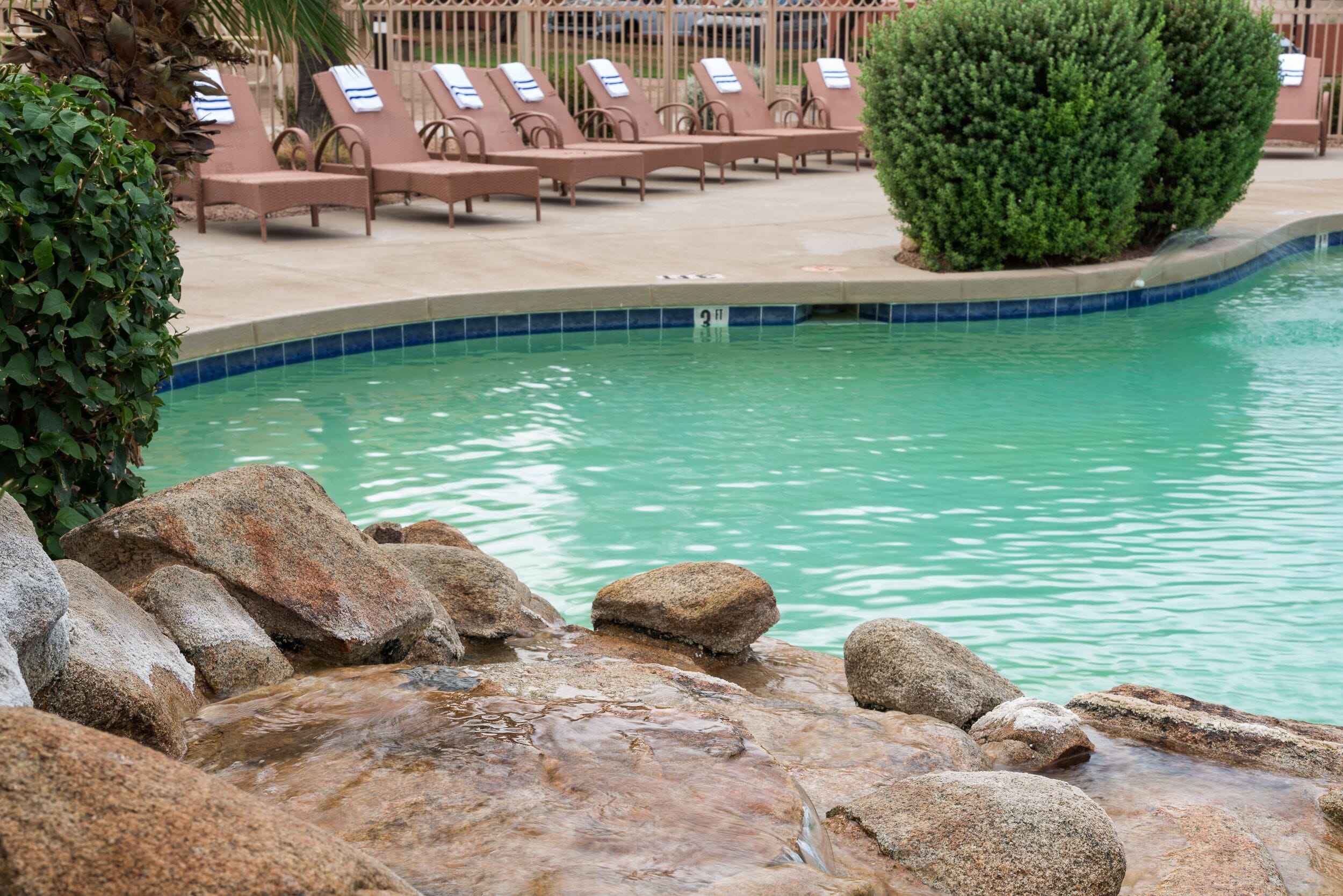Zona de piscina con sillones de descanso y una pequeña cascada.