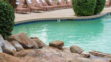 Zona de piscina con sillones de descanso y una pequeña cascada.