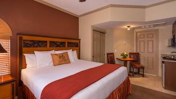 A hotel room with a large bed, a desk, and a kitchenette.