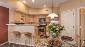 A modern kitchen with a glass dining table, bar stools, and a built-in island with a microwave and oven. - Westgate Painted Mountain Golf Resort (Mesa)