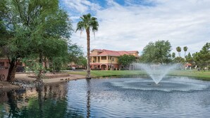 A tranquil pond with a fountain, surrounded by lush greenery and a large building in the background. - Westgate Painted Mountain Golf Resort (Mesa)