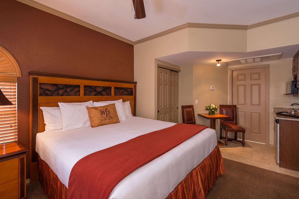 A hotel room with a large bed, a desk, and a kitchenette.