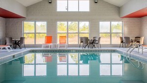A swimming pool with clear water, surrounded by chairs and tables, large windows, and a high ceiling.